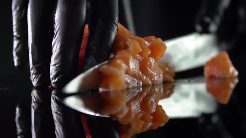 Man with black gloves cuts salmon for sushi in studio