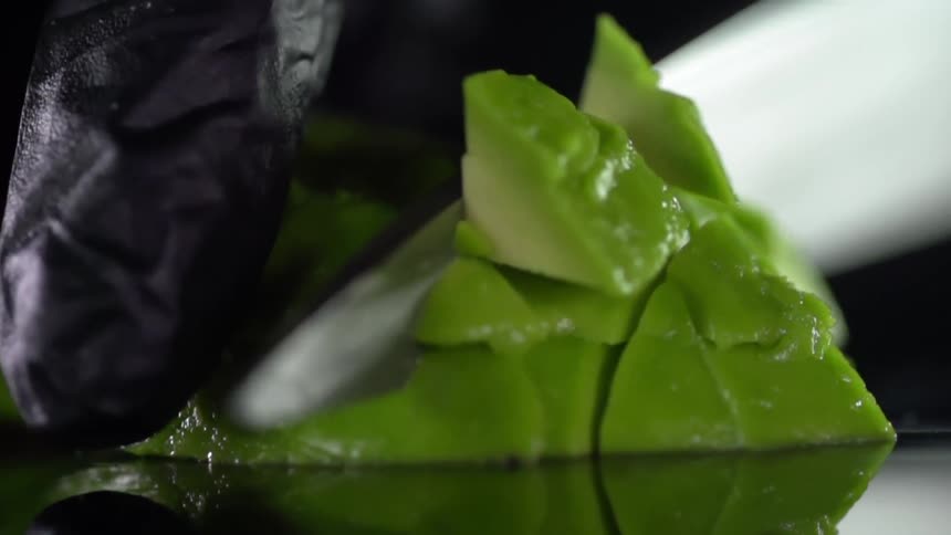 A person holds a pile of sliced avocado and uses a knife to cut in a perpendicular direction