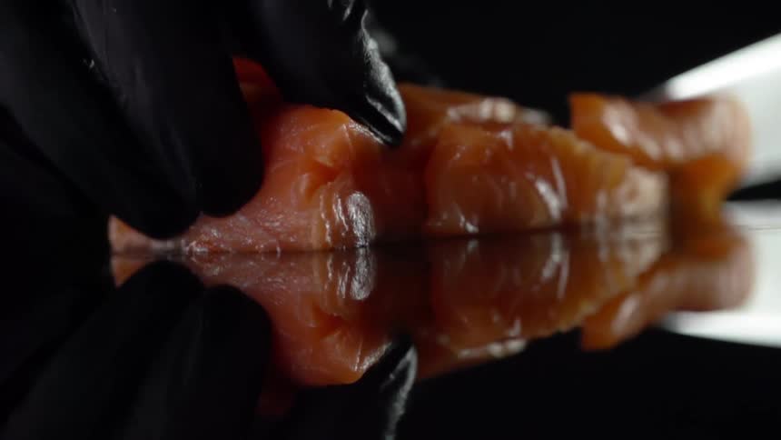 A knife cuts through a piece of raw meat on a reflective surface