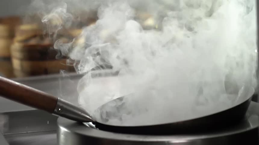 A piece of food falls into a steaming hot wok splashing water