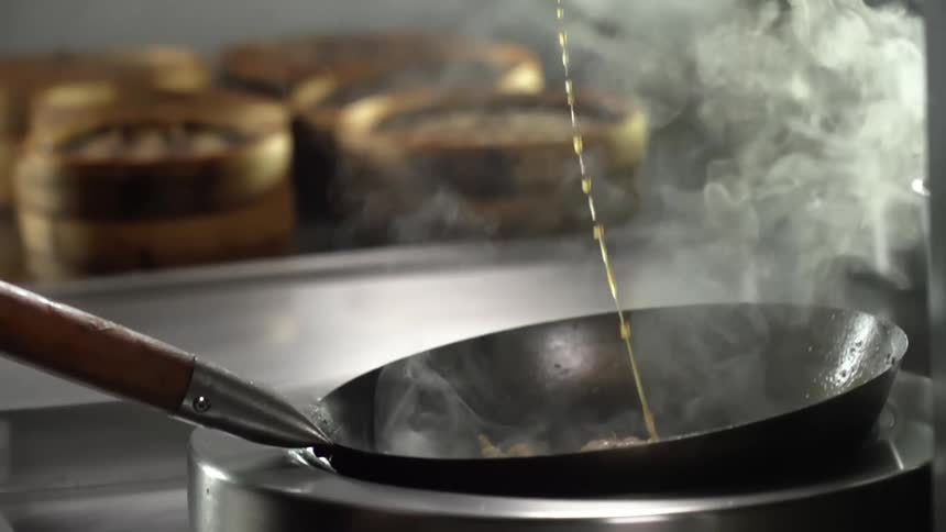 Broth falls into a steaming hot wok in a restaurant kitchen