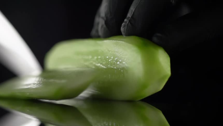 A green vegetable being sliced with a knife while a gloved hand holds it in place