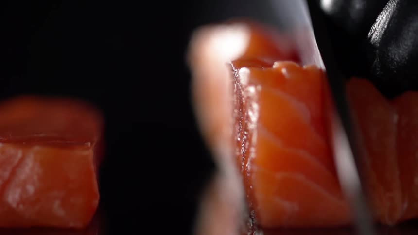 Cook with black gloves slices salmon thinly for sushi