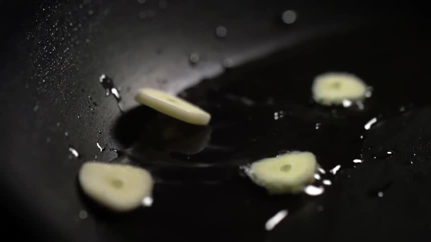 Chopped garlic falling into a pan with oil