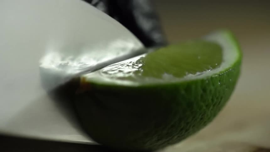 Man wearing black latex gloves slices a lime with a sharp kitchen knife