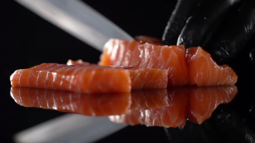 A raw fish fillet being sliced with a knife by a person wearing black gloves