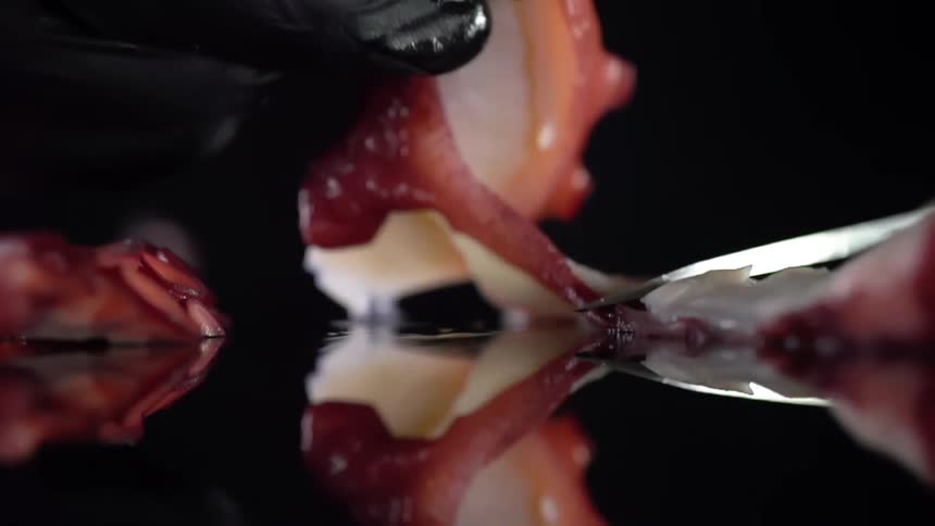 A person wearing a black disposable glove picks up a slice of seafood a dark reflective surface