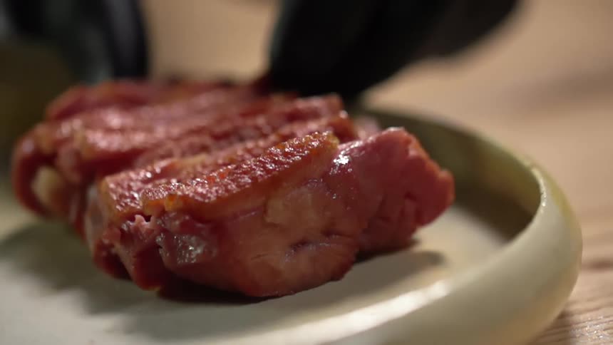 Pieces of cooked beef are carefully placed onto a plate