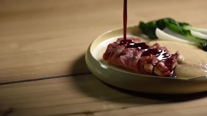 A thick red marinade is poured on slices of pork that sits on a plate with chicken and bok choy