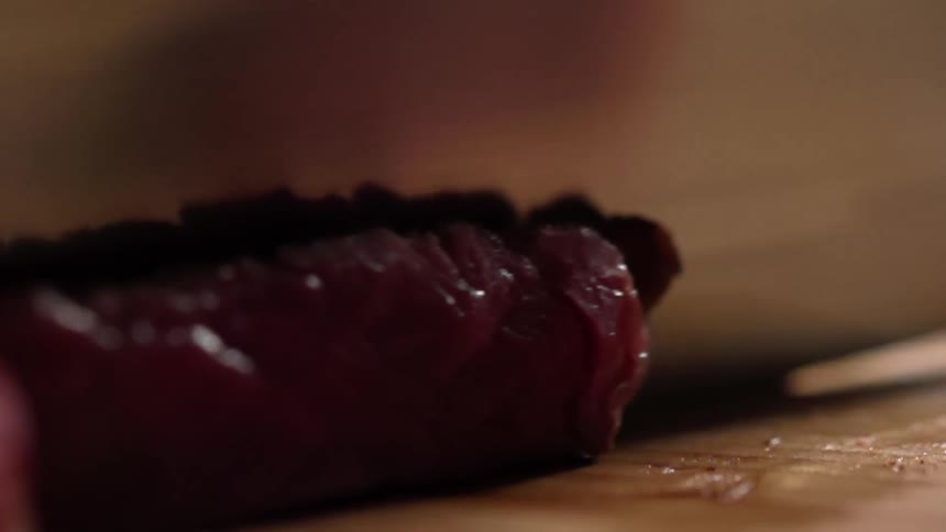 Raw beef is cut with a sharp knife on a wood cutting board