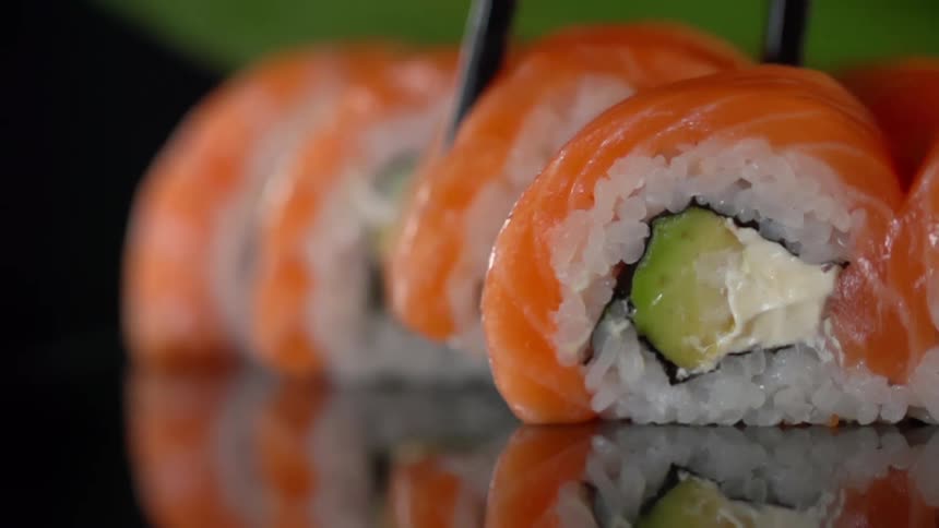 Chopsticks picking up salmon sushi roll from a reflective surface