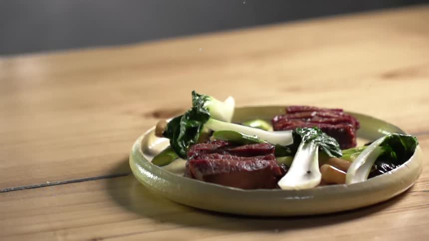 Bok choy falling onto a plate with sliced beef steak on it