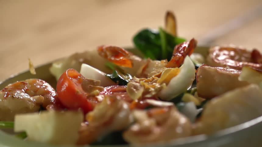 Toppings fall on a plate of shrimps and vegetables