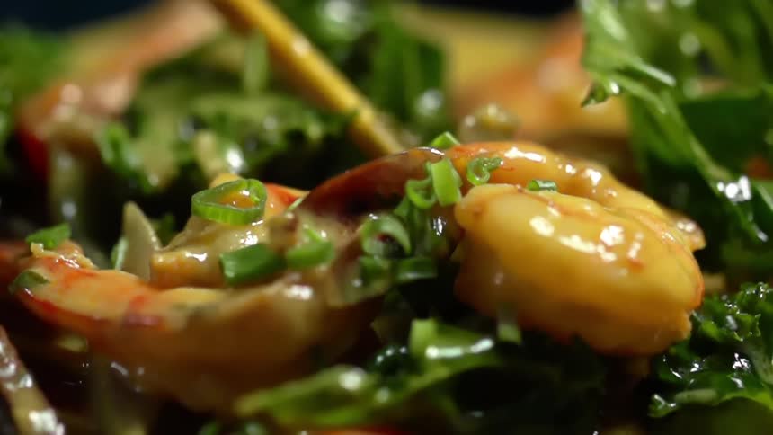 Sliced scallion garnish is dropped on a completed shrimp and vegetable curry