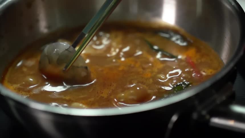 Using chopsticks to dip raw shrimp in the boiling broth inside a metal pot