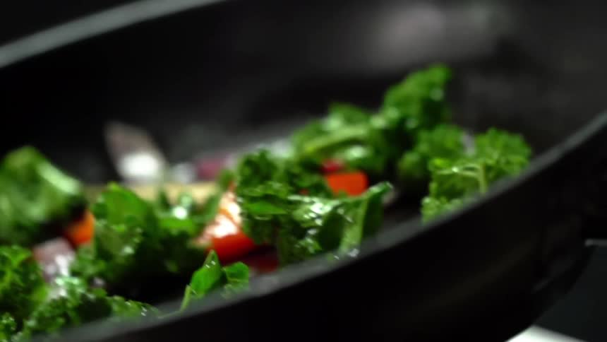 Vegetables being tossed in a cast iron pan while cooking