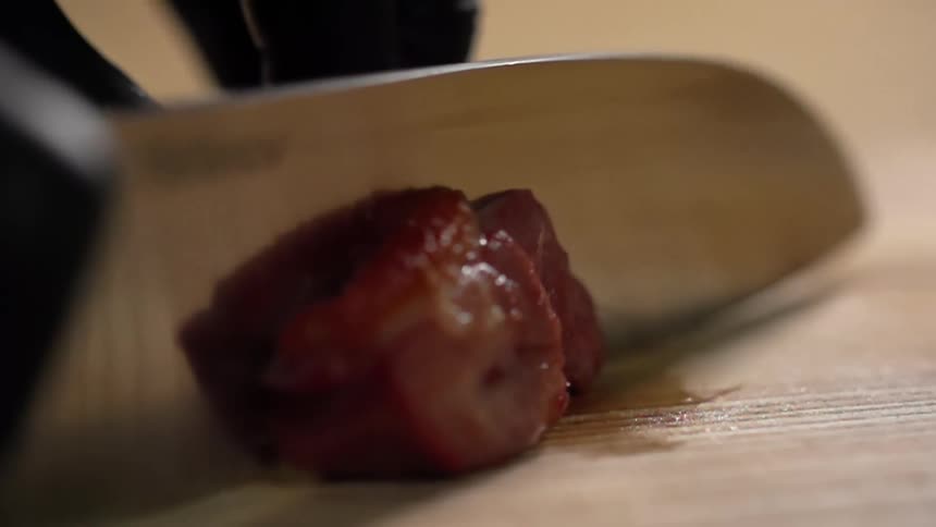 Cook with black gloves cuts beef on a cutting board