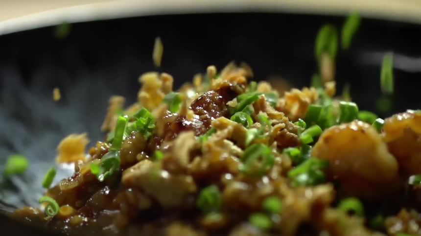 Chopped green onions fall over a dish filled with rice and meat