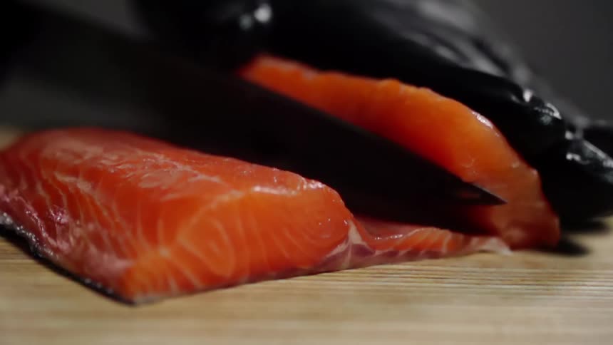 Cook with black gloves cuts salmon for sushi