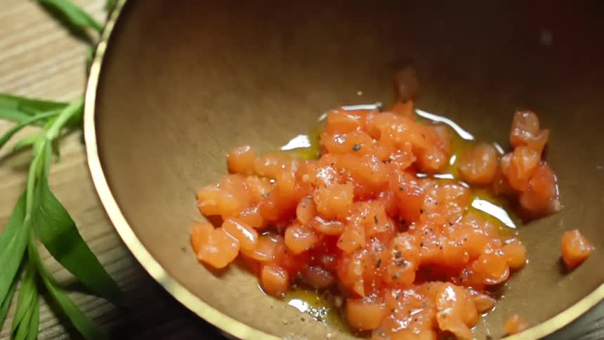 Finely chopped raw salmon being seasoned inside a bowl over a bamboo mat