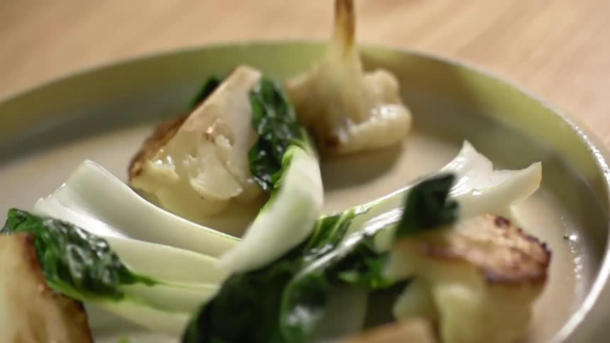 Bok choy is added to a plate of roasted cauliflower