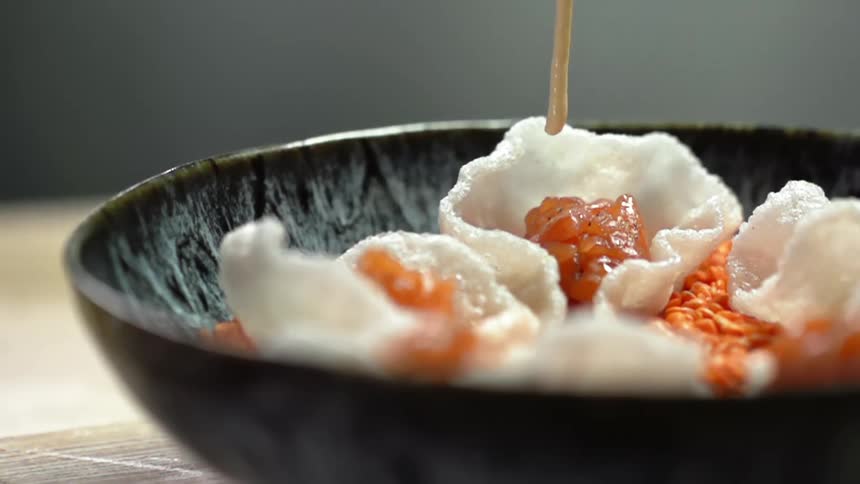 Cream being served on top of salmon in a rice chip in a dark bowl