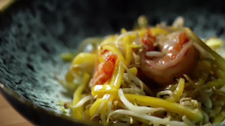 A person putting shrimp with bean sprouts and noodles in a wok