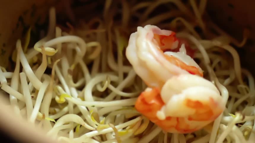 Cooked shrimp falling on a bed of bean sprouts in a bowl