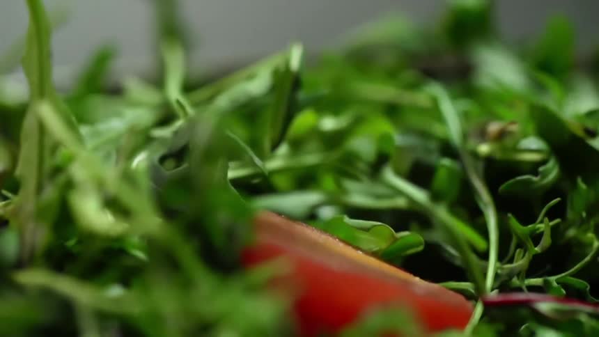 Red tomato slices fall into the leafy green vegetables in a salad