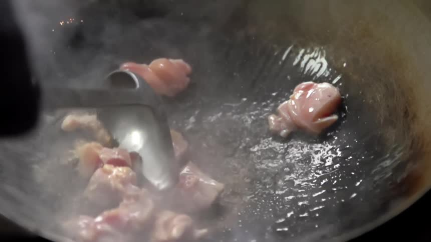 A person wearing black gloves stir frys meat in a wok using a metal ladle