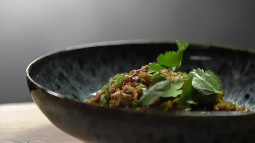 Cilantro falling onto a rice and vegetable bowl on a table