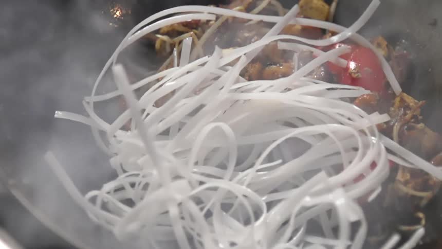 Uncooked rice noodles dropped over vegetables inside a hot steaming wok