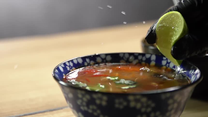 A person squeezing lime into a bowl of soup