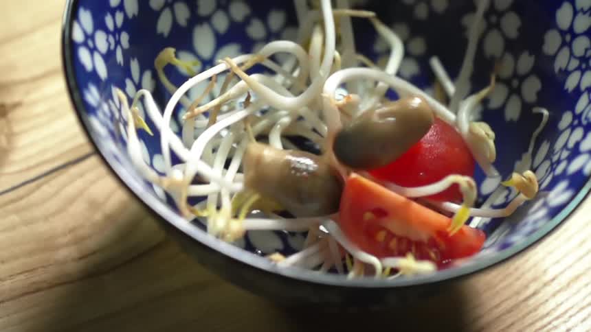 Mushrooms falling into a bowl with tomatoes and bean sprouts in it