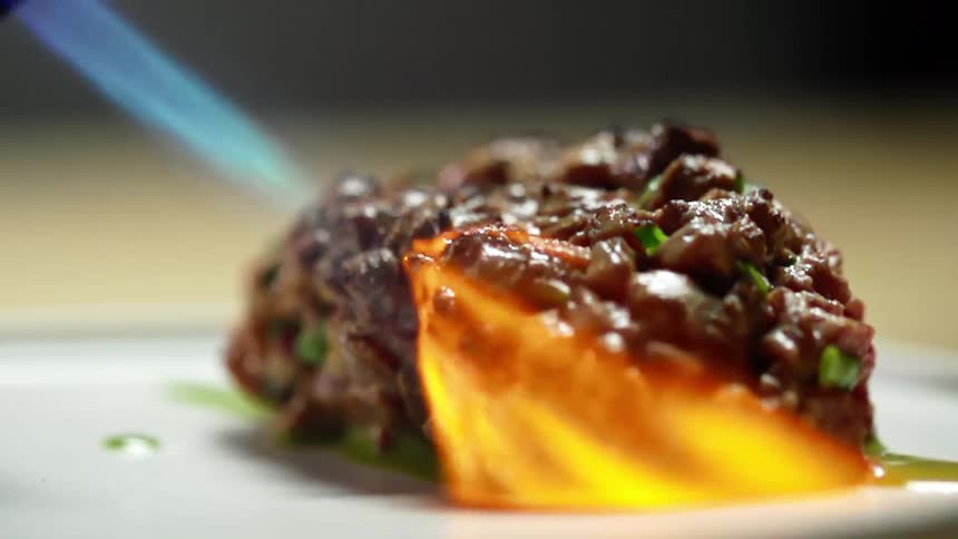 A torch sears chopped and diced tuna on a plate