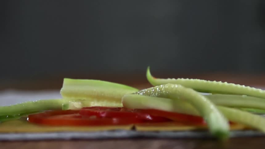 Vegetables falling atop a stack of cheese and tomatoes on a cloth