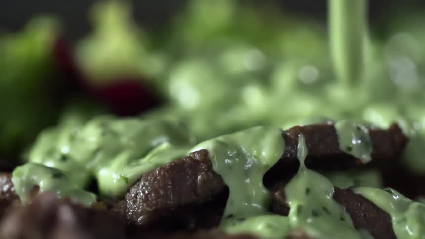 A green cream falling onto meat