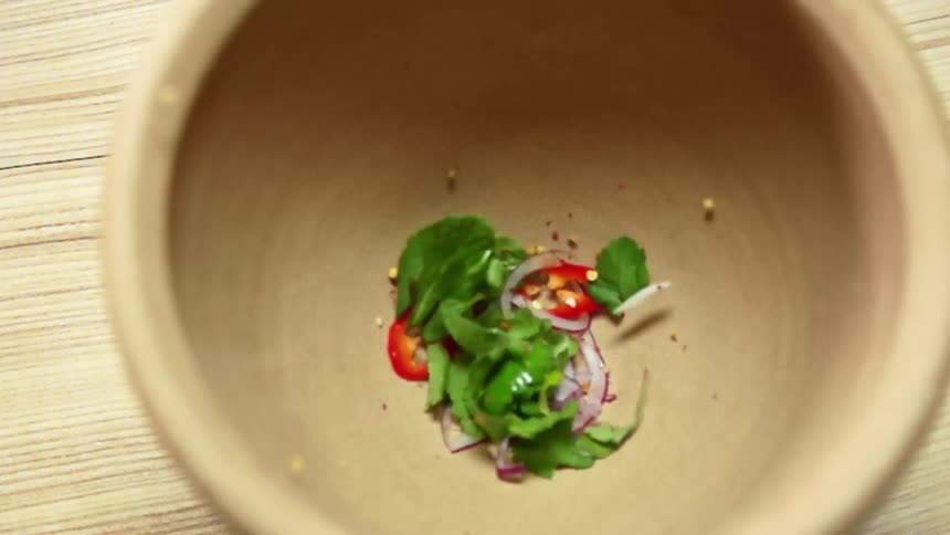 Sliced red pepper onion and cilantro leavs are dropped into an empty mortar