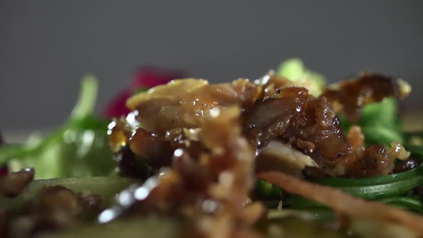 Several thin pieces of moist grilled meat are sprinkled atop a pile of salad