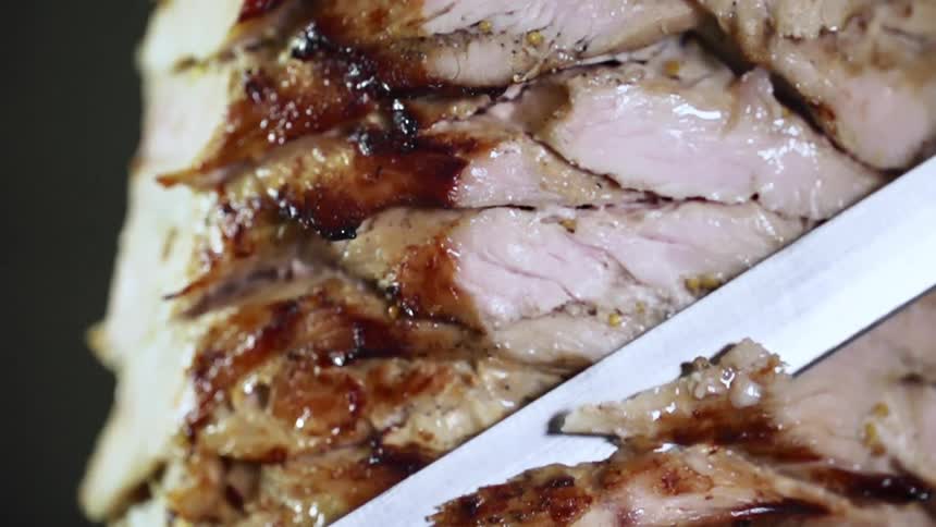 Chef wearing black latex gloves cuts meat from a kebab using a sharp kitchen knife