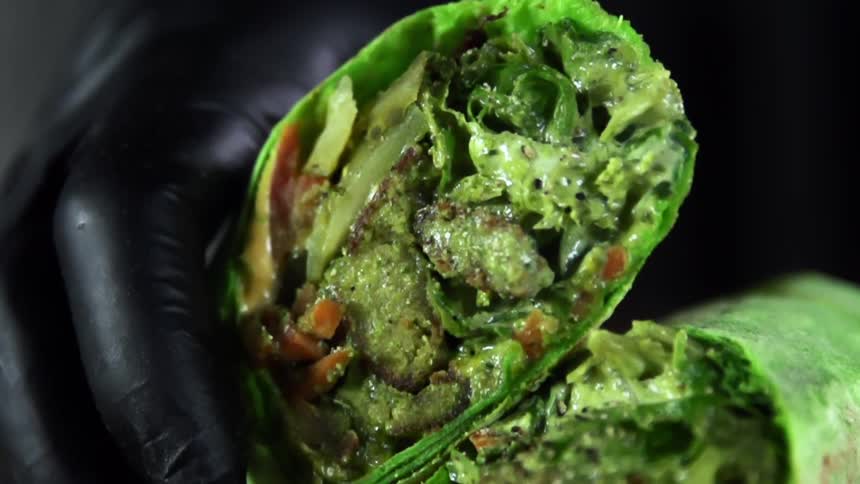 A person with black gloves putting down a wrap with vegetables
