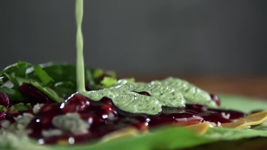 Green creamy sauce pouring onto a plate with sauces and vegetables