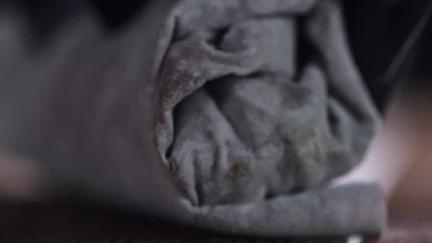Chef wearing black latex gloves rolls a grey flour tortilla