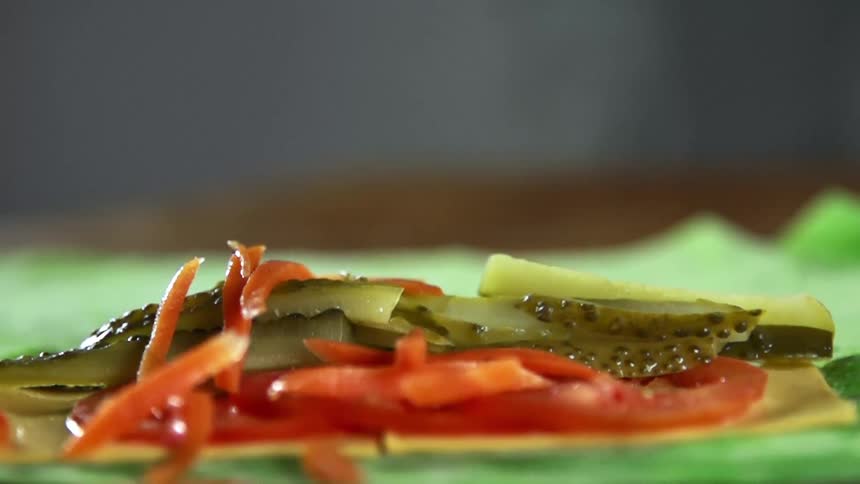 Thin carrot sticks drop onto tomato and pickle slices covering sliced cheese