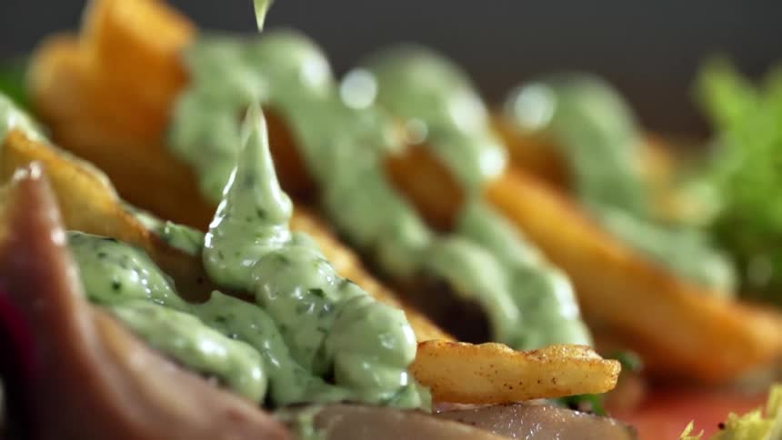 Green sauce pouring over fried potatoes in a dish
