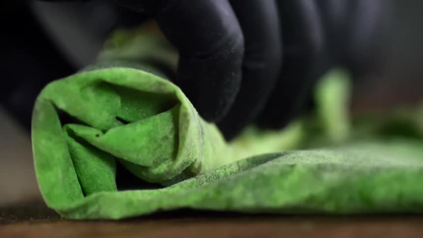 Person wearing black gloves rolls folded green item