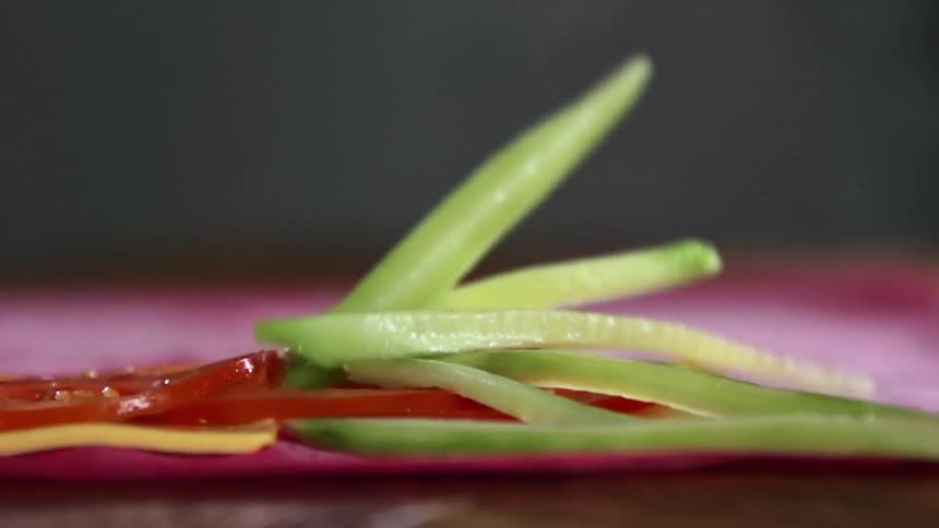 Strips of cucumber fall on cheese and tomatoes