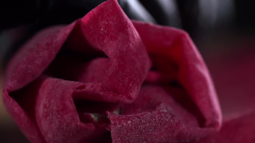 A red colored flat bread is rolled into a wrap by gloved hands