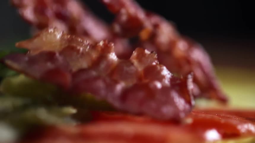 Cooked bacon falls onto some vegetables