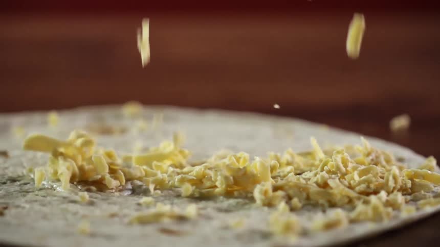 Grated cheese falling into a flour tortilla in a wooden table